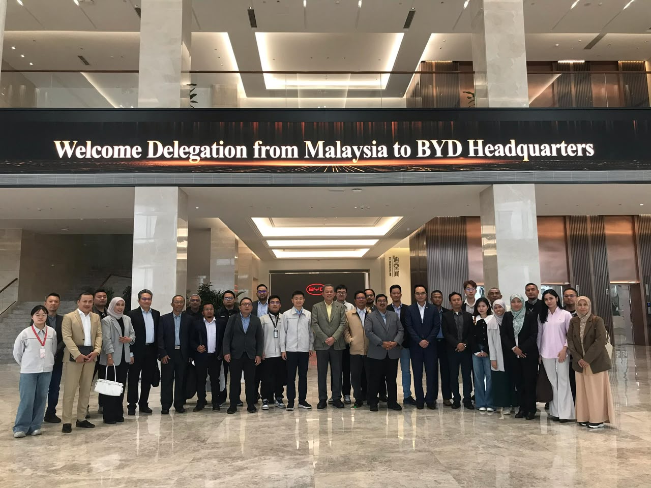 About forty members of the delegation in a marble lobby under a screen reading Welcome Delegation from Malaysia to BYD Headquarters.