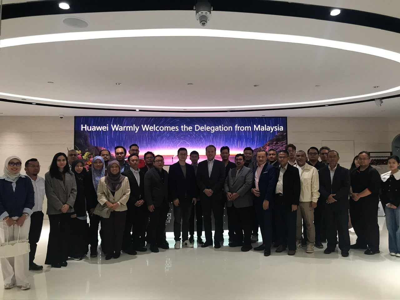 About forty members of the delegation inside Huawei, under a screen reading Huawei Warmly Welcomes the Delegation from Malaysia.