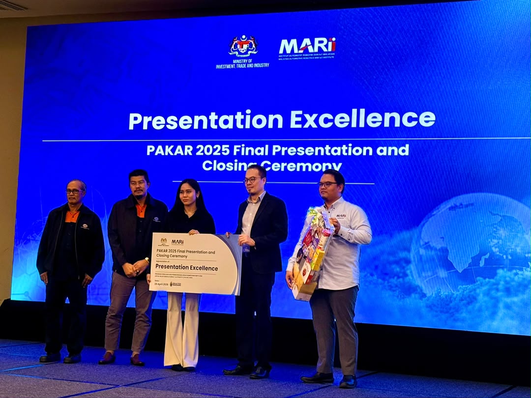 SBI's representative on stage holding a board reading Presentation Excellence, beside the presenters, under a screen for the PAKAR 2025 Final Presentation and Closing Ceremony.