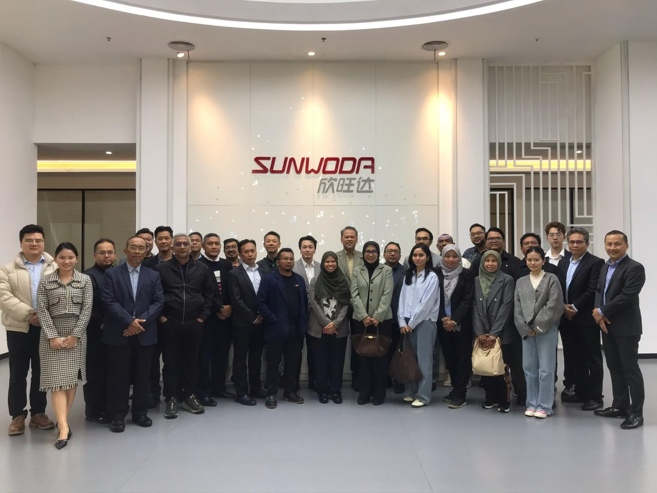 About thirty members of the delegation in a lobby in front of the Sunwoda logo.