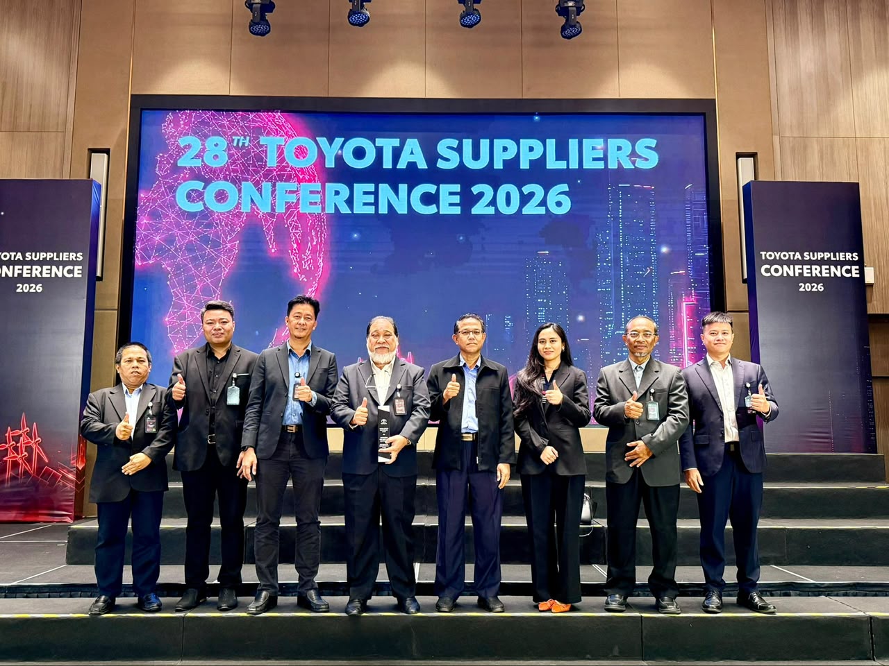 Eight people giving a thumbs-up on stage in front of a screen reading 28th Toyota Suppliers Conference 2026.