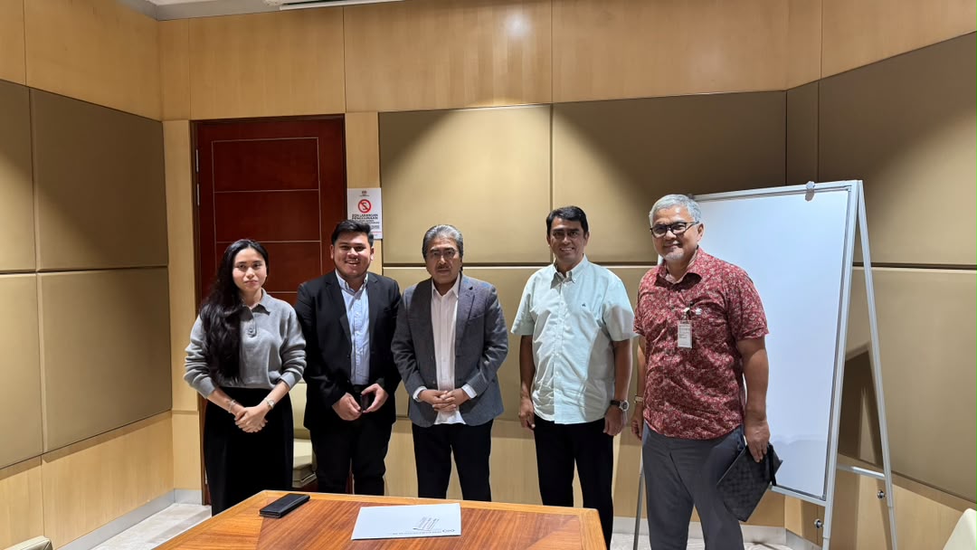 Five people, SBI's team with Dato' Sri Johari Abdul Ghani, standing in a wood-panelled meeting room behind a low table.
