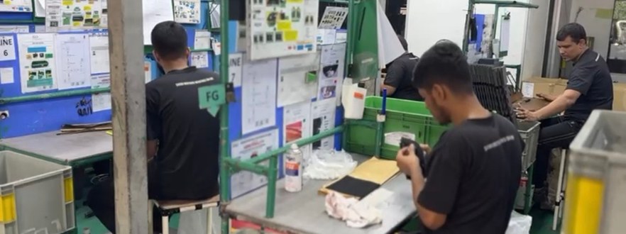 Operators at assembly stations, each with a work instruction sheet posted above the bench.