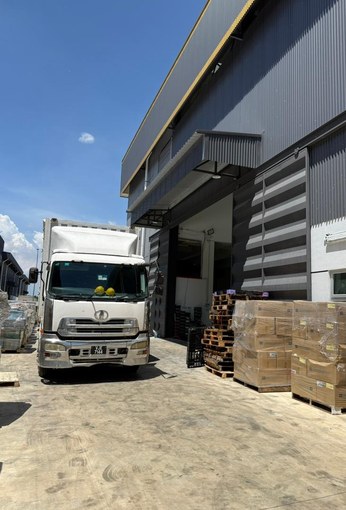 A lorry at the loading bay beside the plant, with cartons stacked on pallets next to it.