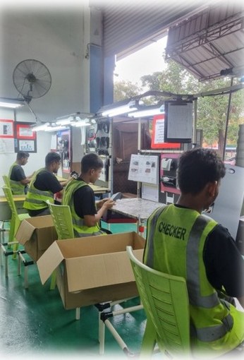Inspectors in high-visibility vests seated at a row of tables, checking parts from cartons.