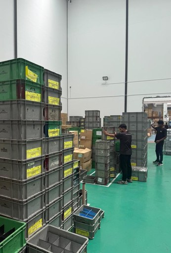 Green and grey plastic crates stacked high in the storage area, with two workers moving stock.